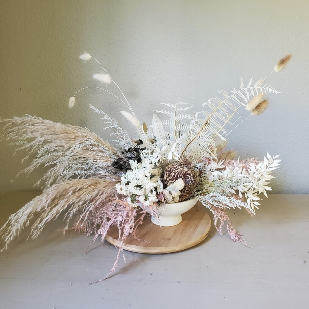 Alma dried floral arrangement in a white bowl with pampas grass and neutral-toned foliage on a wooden board