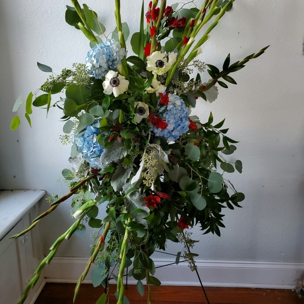 Beloved sympathy standing spray with blue hydrangeas, white anemones, red accents, and lush greenery