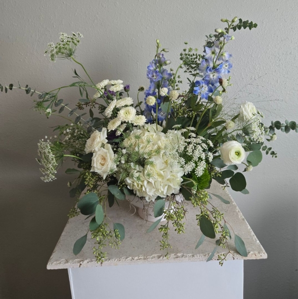 Brianna floral arrangement with white hydrangea, roses, blue delphinium, and eucalyptus in a low vase