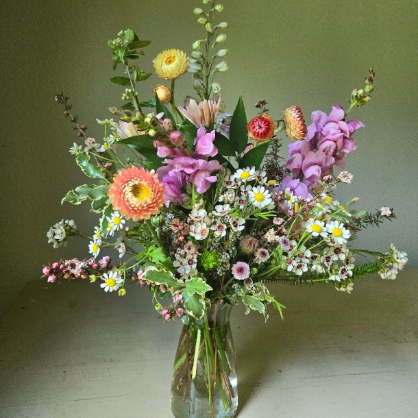 Dainty floral arrangement in a glass vase with pastel blooms, daisies, and greenery