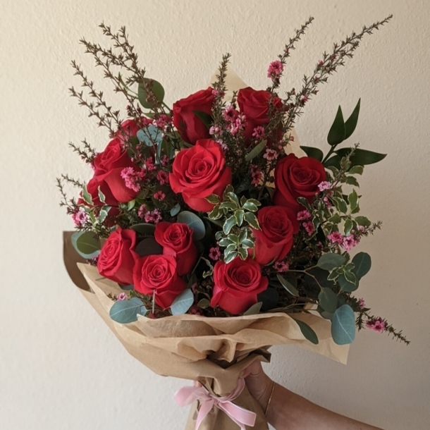 Wrapped bouquet of a dozen red roses with greenery and small pink filler flowers