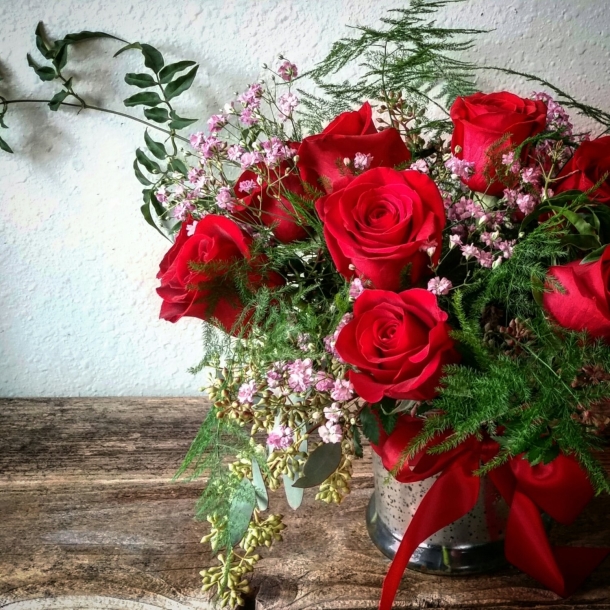 Dozen red rose arrangement with greenery and baby's breath in a vase with red ribbon