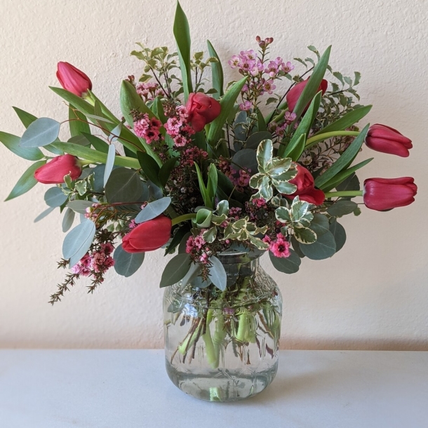 A dozen red tulips arranged with mixed greenery and pink filler flowers in a clear glass vase