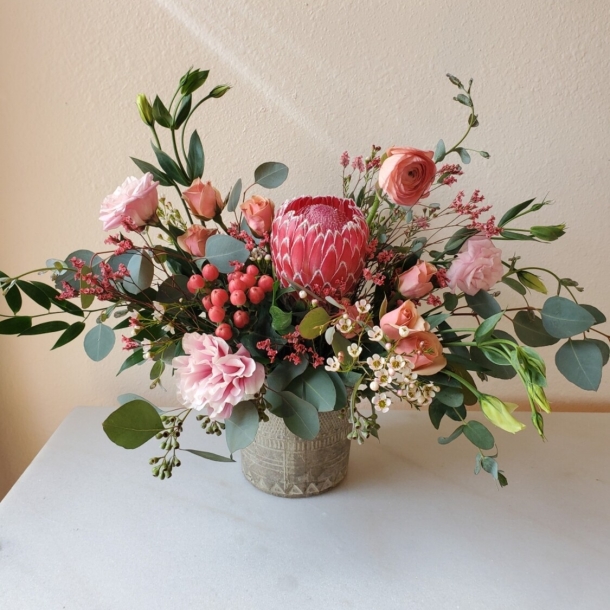 Dullaney floral arrangement with pink protea, roses, eucalyptus and berries in a ceramic vase