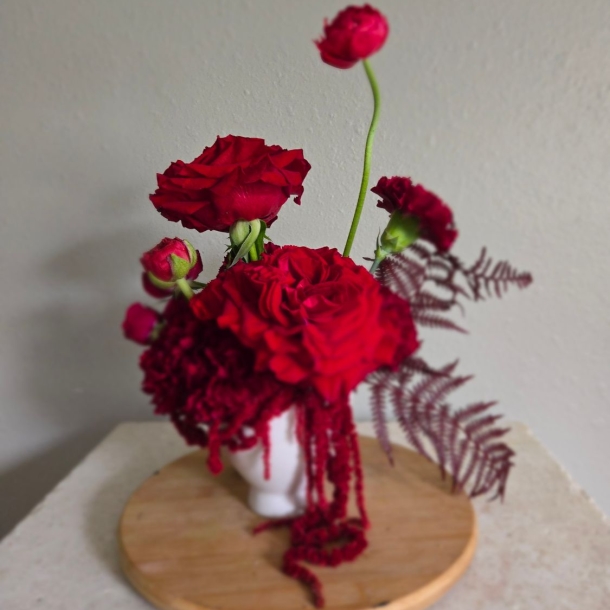 Emma floral arrangement with red blooms in a white vase on a wooden stand