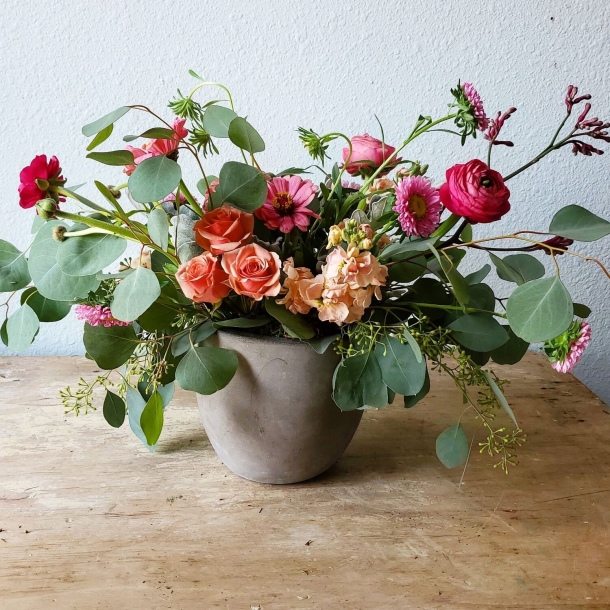 Esther floral arrangement with coral roses, pink ranunculus, and eucalyptus in a gray ceramic bowl