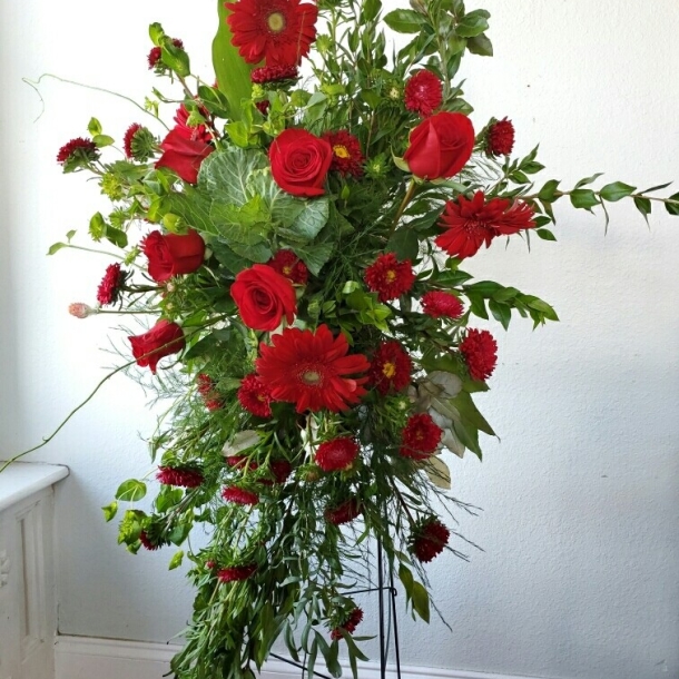 Forever sympathy standing spray with red roses, red gerbera daisies, and greenery