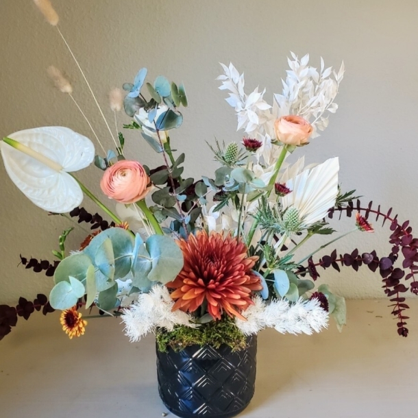Glory floral arrangement with peach and white blooms, eucalyptus, and burgundy accents in a black textured vase