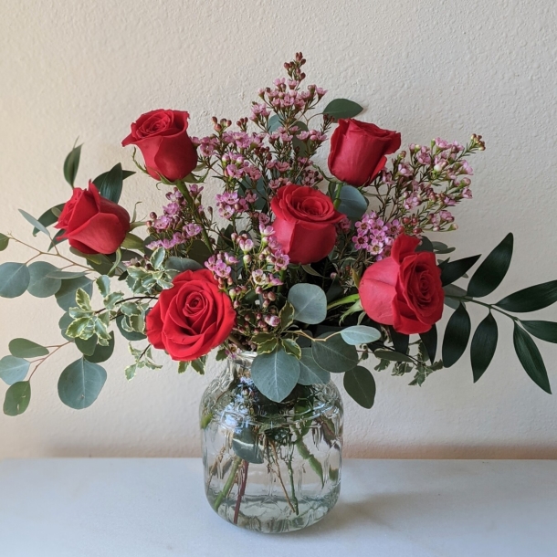 Half dozen red roses arrangement in a clear glass vase with pink filler flowers and eucalyptus greenery