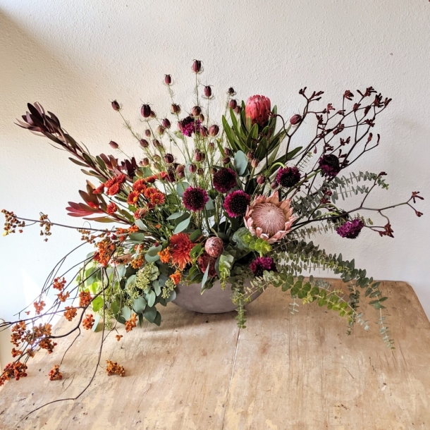 Lavish floral arrangement with protea, wild blooms, and eucalyptus in a low bowl centerpiece