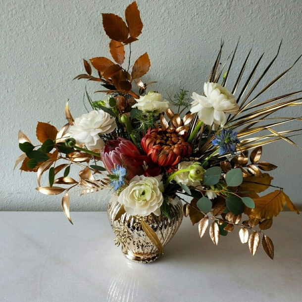 Olivia floral arrangement in gold vase with white blooms, protea, and metallic foliage