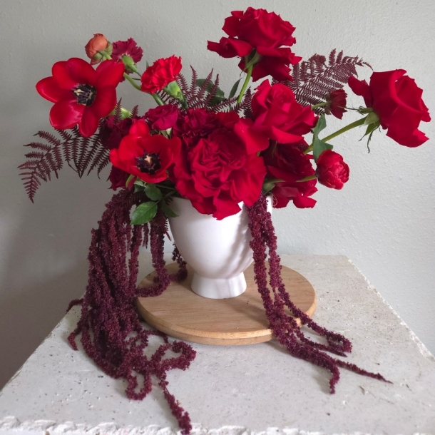 Rosalie floral arrangement with red roses and blooms in a white vase with cascading burgundy amaranthus