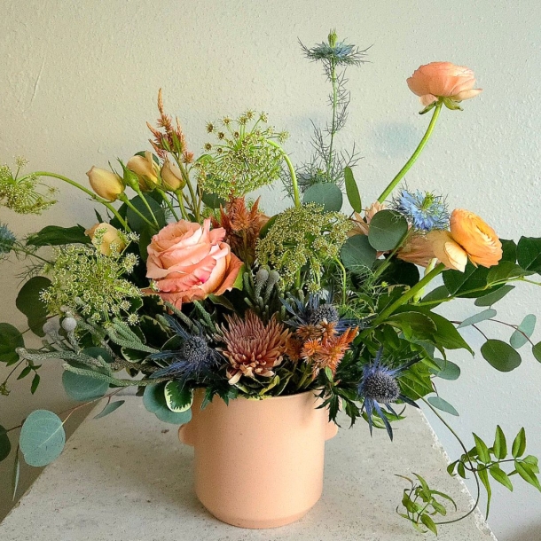 Sasha floral arrangement in a blush ceramic pot with peach blooms, blue thistle, greenery, and eucalyptus